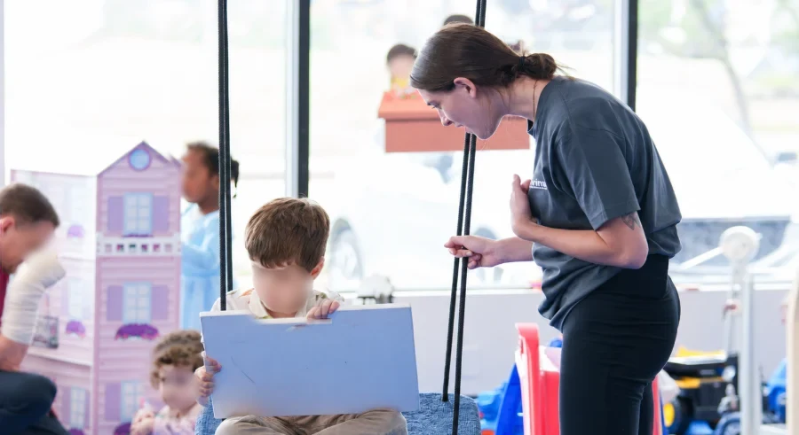 A Care Specialist talking with a boy on a platform swing