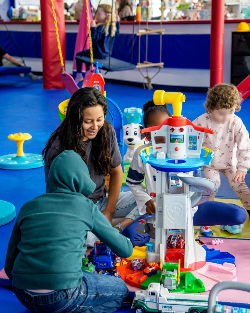 A Care Specialist smiling as children play with a toy lookout tower